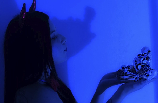 Halloween con Isabella Salcedo: elegancia, fuego y deseo | Sagitariux Mujer en un cuarto azul, con una calavera blanca, vestida de diablita, mostrando actitud y un aire seductor en Halloween